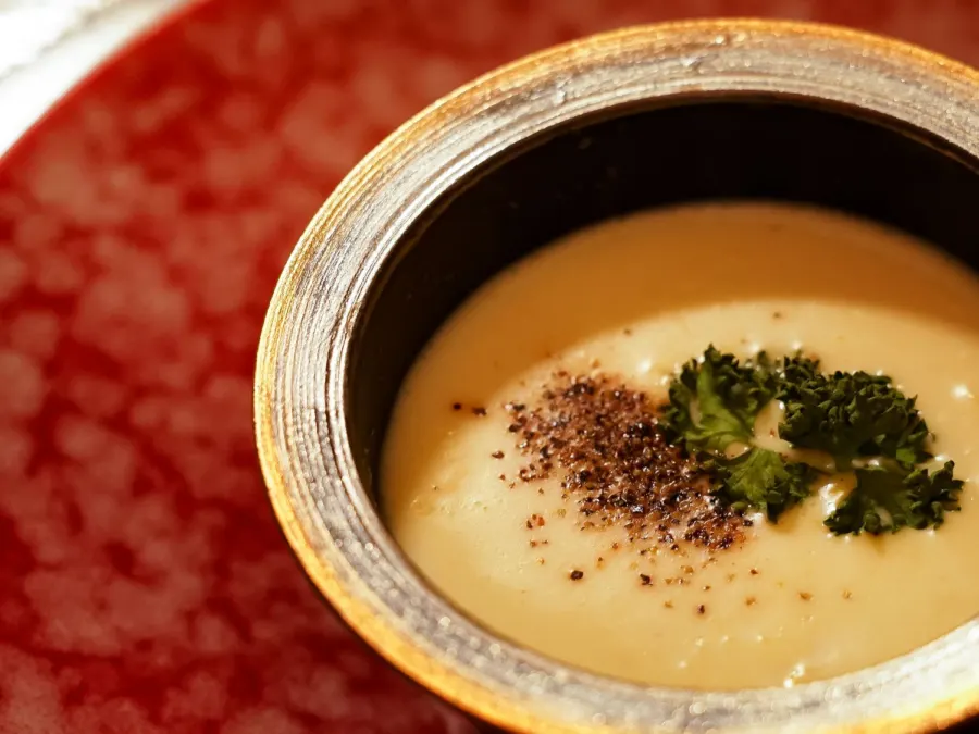 A seasonal purée soup in a vermilion bowl